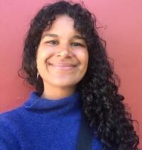 a female student researcher with dark long curly hair smiling